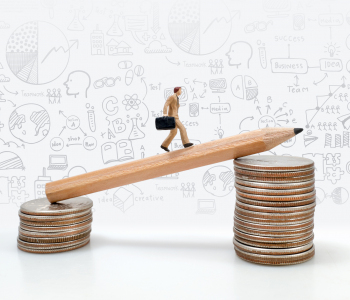 Die Miniatur-Figur eines Businessmannes balanciert auf einem Bleistift, der zwischen zwei Münzstapel hängt.